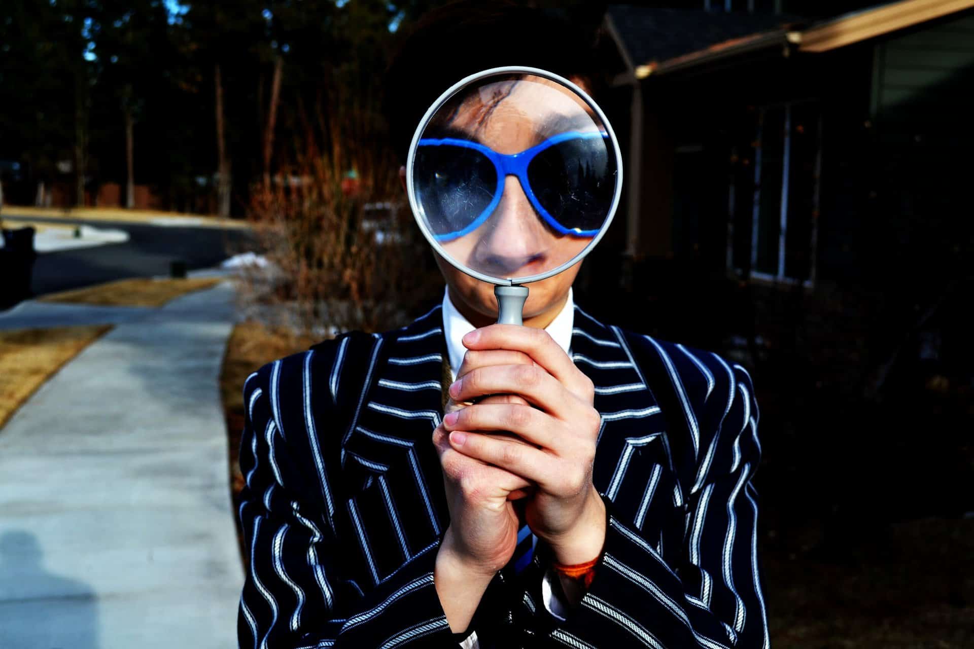 person in a suit with blue sunglasses looking through a magnifying glass