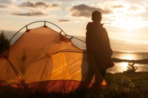 person standing next to tent camping with the sunrise